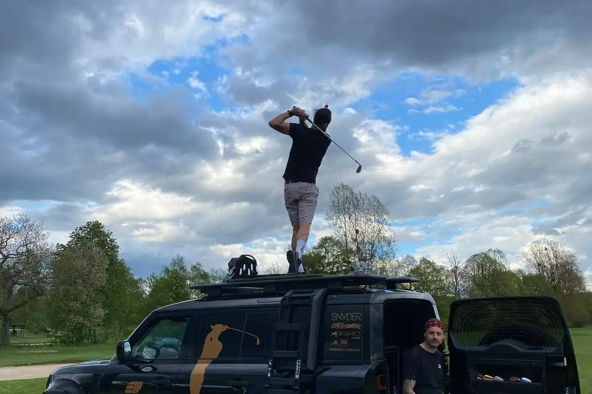 Golfer beim Abschlag vom Defender-Dach unter dramatischem Himmel
