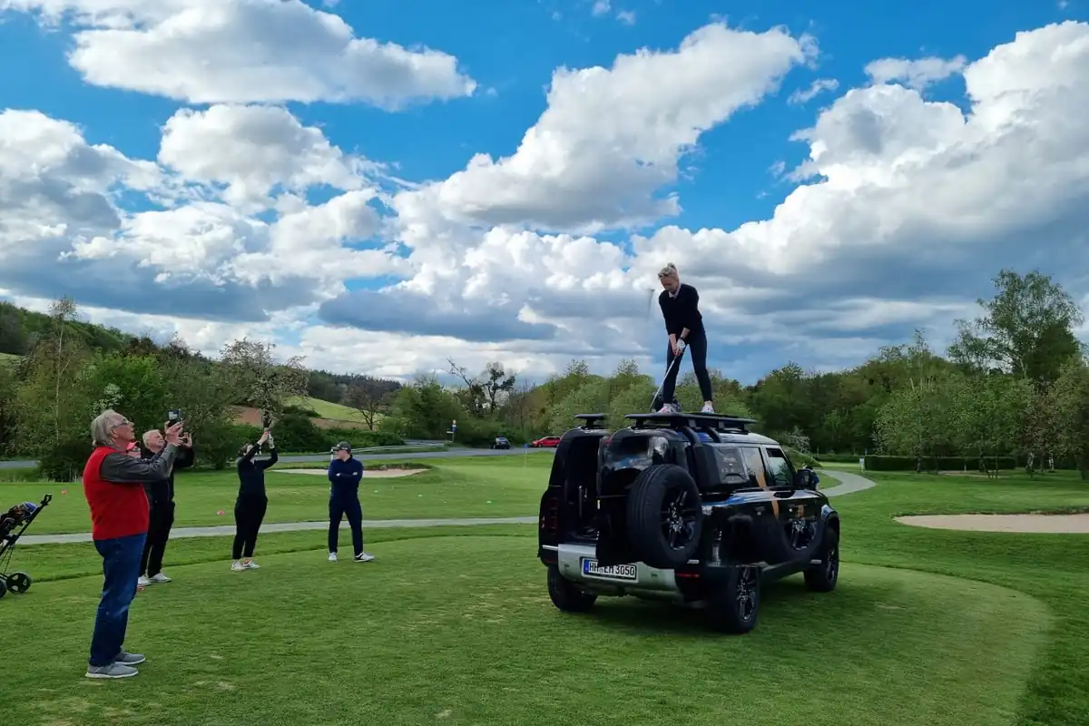 Golferin beim Abschlag vom Defender-Dach mit Zuschauern auf dem Golfplatz