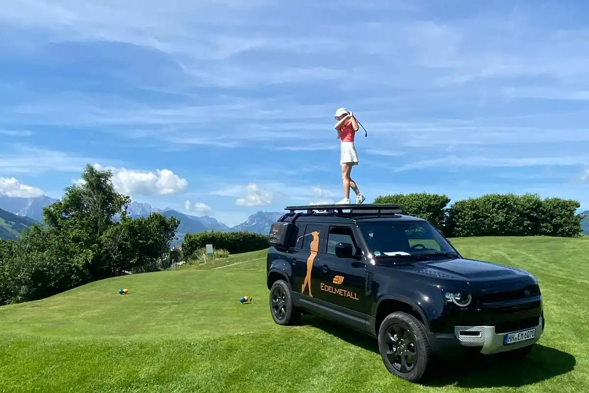 Golferin auf dem Defender-Dach vor Alpenpanorama beim Golfturnier